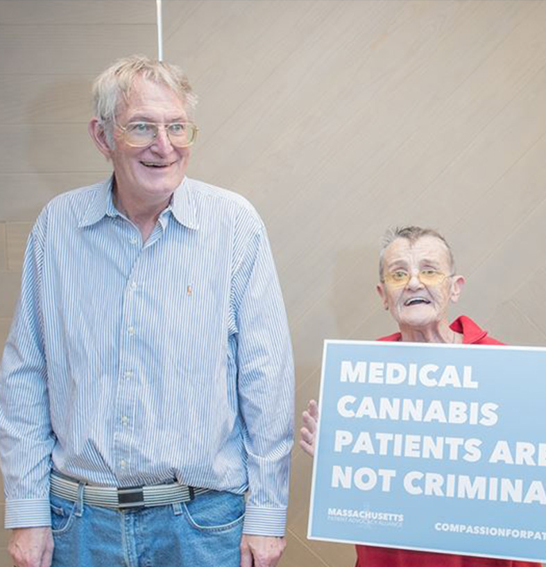 Two hardship patients standing together with one holding a sign that reads medical cannabis patients are not criminals